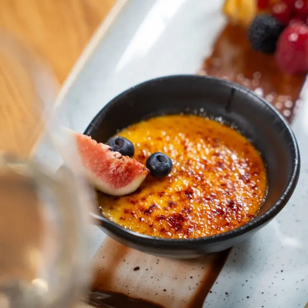 Creme brûlée i sort skål toppet med figen og blåbær på serveringsfad.
